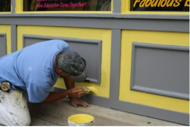 Man painting store front with yellow and gray paint